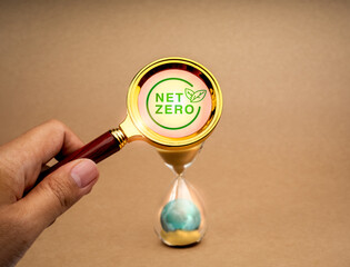 Reaching net zero, Carbon emissions reduction plan and time management concept. Net Zero symbol through magnifying glass lens on hourglass with 3d earth globe inside, on recycle paper background.