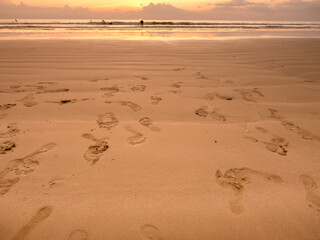 Many leaving footprint on sand beach with sunset sky background. Close-up many people's footprints from foot step walking variety direction on the wet sand. Beach travel, summer background concept.
