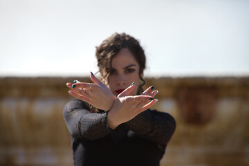Beautiful woman dancing flamenco in a square in Seville, Spain. She wears a typical black dress and shows her hands strongly to the camera. Focus on hands and face out of focus. - obrazy, fototapety, plakaty