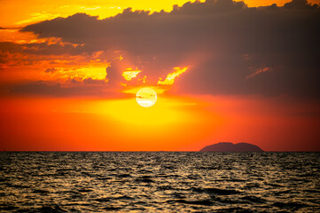 fiery sunset over ocean, with vibrant shades of orange and red painting sky. sun sets dramatically,...