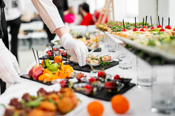 A skilled caterer meticulously arranges a variety of delectable appetizers on a table at an event,...