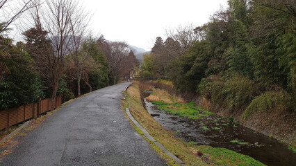 Yufuin, Japan - 01.25.2020: A riverside path on a rainy day with pedestrians walking along the river and trees