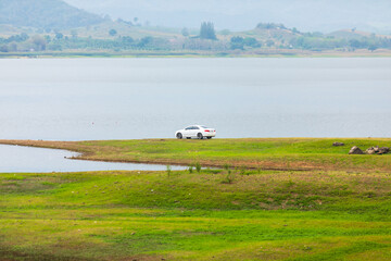 White sedan car parking near the lake water. with beautiful green grass.