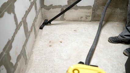 A worker vacuums a concrete floor. Worker washes the floor with a vacuum cleaner from industrial...