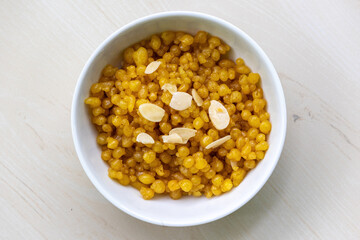 Traditional tiny sweet Bundiya on a white bowl on wooden background. It is also known as boondi, burinda, and buniya. Popular Bengali (Bangladesh) food for weddings and festivals. Top view.