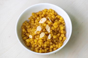 Delicious tiny sweet Bundiya on a white bowl on wooden background. It is also known as boondi, burinda, and buniya. Traditional Bengali (Bangladesh) food for weddings and festivals.