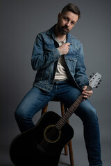 Studio portrait of a handsome caucasian man in his 40s holding an acoustic guitar sitting on a...