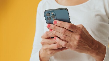 Close-up of hands of young woman using mobile phone isolated on yellow background in studio