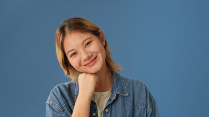 Close-up of young smiling woman dressed in denim shirt isolated on blue background in studio