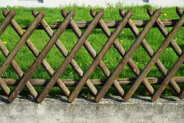 Brauner alter Jägerzaun aus Holz über grauer Steinmauer vor grüner Wiese im Garten und weißer...