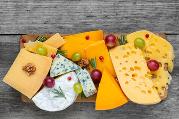 Assortment cheeses on wooden cutting board. Cheese plate served with grape fruits, pomegranate and rosemary, various cheese on a platter. top view - 778815761