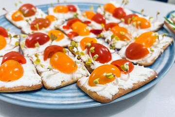 Close crackers spread with soft cottage cheese with cherry tomatoes cut in half and decorated with micro greens. side view. Snack for children. healthy food. holiday in kindergarten