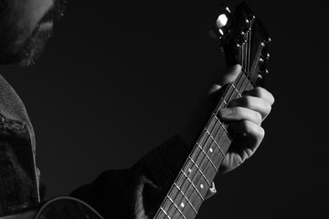 Close up photo of a caucasian hand holding an acoustic guitar. The man is wearing a jean jacket. 