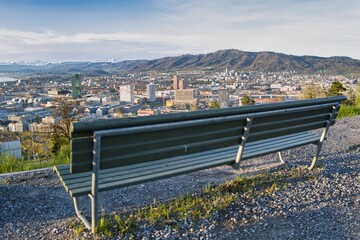 Park bench with a view of the city of Zurich in spring with the snowy Swiss Alps in the background from the Waid - obrazy, fototapety, plakaty