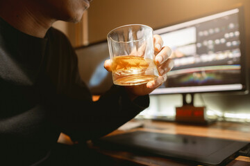 Asian male movie video editor or colorist relaxing with a whisky, successfully working with footage...
