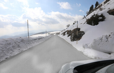 slippery mountain road with snow on the sides and posts to mark the limit of the roadway seen from...