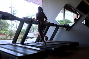 silhouette of excited woman exercising on treadmill machine, back view of asian woman running on...
