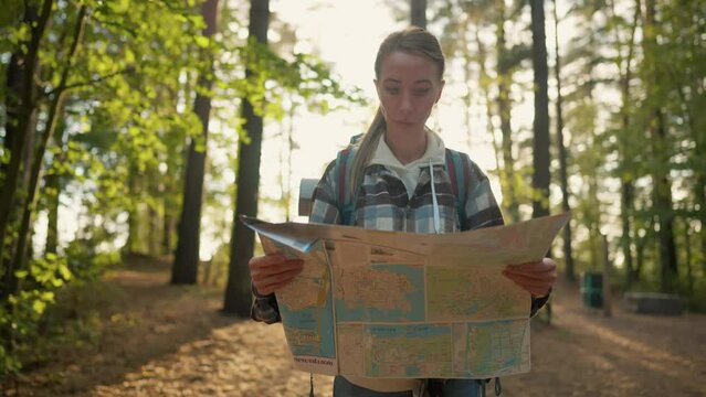 Woman hiker hiking with map in forest. Female tourist finding route way looking at paper map walking on nature in woodland. Trekking carrying backpack. Travel tourism trekking navigation concept.