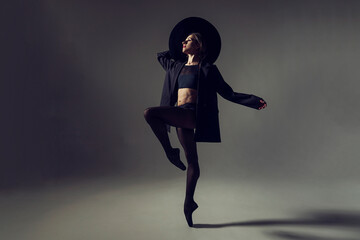 ballerina in the style of fashion total black in a jacket and hat poses ballet elements