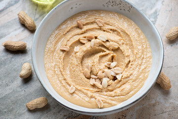 Grey bowl with peanut butter or paste made from ground, dry-roasted peanuts, middle closeup, horizontal shot, selective focus