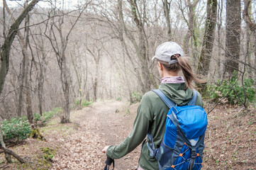 Woman tourist with backpack and walking stick hiking the forest path