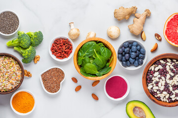 Assortment of various super foods for clean eating antioxidant detox diet on white background. Spinach, ginger, berries, seeds, powder, beans, mushrooms and nuts. Balanced nutrition concept. Top view