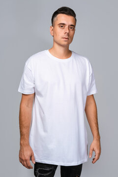 Man dressed in a white oversized t-shirt with blank space, ideal for a mockup, set against gray background