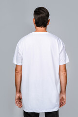 Man dressed in a white oversized t-shirt with blank space, ideal for a mockup, set against gray...