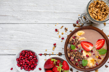 Chocolate smoothie bowl with oat granola, banana, strawberries and pomegranate seeds on white wooden table. Top view with copy space. Healthy vegan protein food for breakfast - 778878518