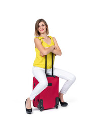 A happy young woman in a yellow T-shirt and white trousers is sitting on a red suitcase waiting, isolated on a white background