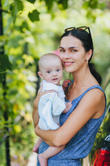 A beautiful young smiling brunette woman holds a small child, her son, in her arms outdoors in...