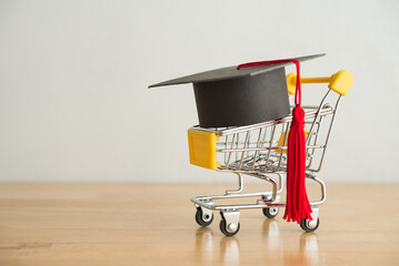 Graduation cap university or college degree in shopping trolley on wooden table white wall background copy space. Job fair, recruitment, employee search vacancy jobs, employer search resume concept.
