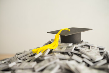 Graduation cap university or college degree on US dollars banknotes pile. Education expense budget...