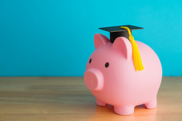 Pink piggy bank and mortarboard on wooden table with blue background copy space. Money savings and...