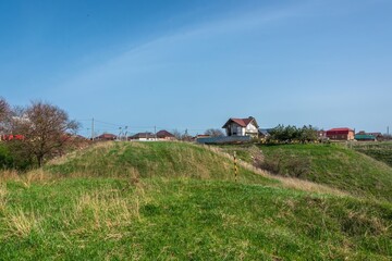 a hill overgrown with green grass on the site of an ancient citadel surrounded by a moat near a village in the vicinity of the city of Ust-Labinsk (South Russia) on a sunny spring day