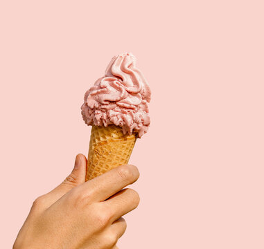 Hand holding strawberry ice cream cone isolated on pink background.