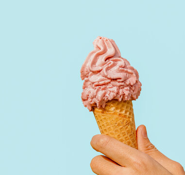 Hand holding strawberry ice cream cone isolated on light blue background.