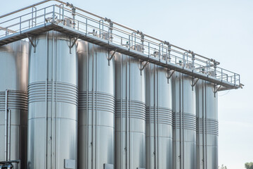 Close up of stainless vertical steel storage tanks for wine fermentation and maturation in modern winery factory production. Industrial and technology textured background