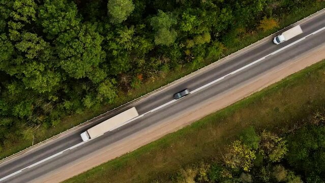 Diagonal drone or aerial view on tracks and driving cars on the road between trees. 4K resolution video. The drone hovers over a busy road in the forest.