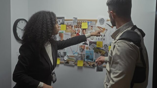 A man and a woman, both investigators, discuss a case in a police department's evidence room, surrounded by photos and clues.
