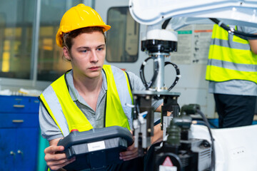 Manufacturing industry factory manufacturing technology concept. Professional male technician engineer in safety wear checking robotic machine arm system in production line for repair and maintenance.