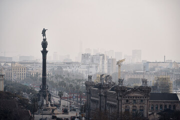 La ciudad de Barcelona vista desde la montaña con el monumento de Cristóbal Colón en el skyline de la ciudad bajo la niebla. - obrazy, fototapety, plakaty