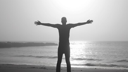 Fototapeta premium A man stands with his arms outstretched on the beach sunset, silhouette style, monotone black-white