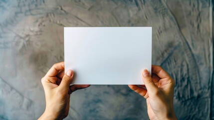 Hands holding a blank white sheet of paper on a gray background
