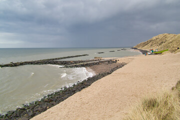 Beach with shore protection, dark and cloudy sky and sand dunes with grass