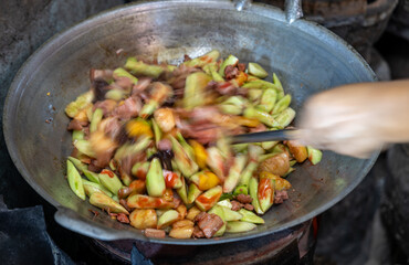 Close-up, blurry motion of a female cook's hand roasting and stir-frying pork.