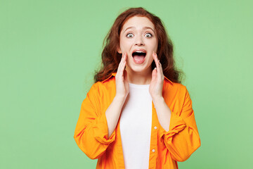 Young ginger woman wear orange shirt white t-shirt casual clothes scream sharing hot news about sales discount with hands near mouth isolated on plain pastel light green background. Lifestyle concept.