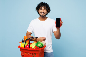 Young Indian man wear white t-shirt casual clothes hold basket takeaway mock up with food products use blank screen area mobile cell phone isolated on plain blue background Delivery service from shop - Powered by Adobe