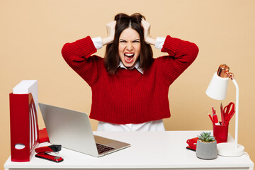 Young sad mad stressed employee business woman wear red sweater shirt sit work at office desk with...