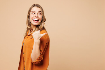 Young smiling happy Caucasian woman she wears orange shirt casual clothes point thumb finger aside...